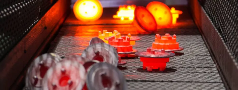 Pièces métalliques incandescentes sur un convoyeur pour traitement thermique.