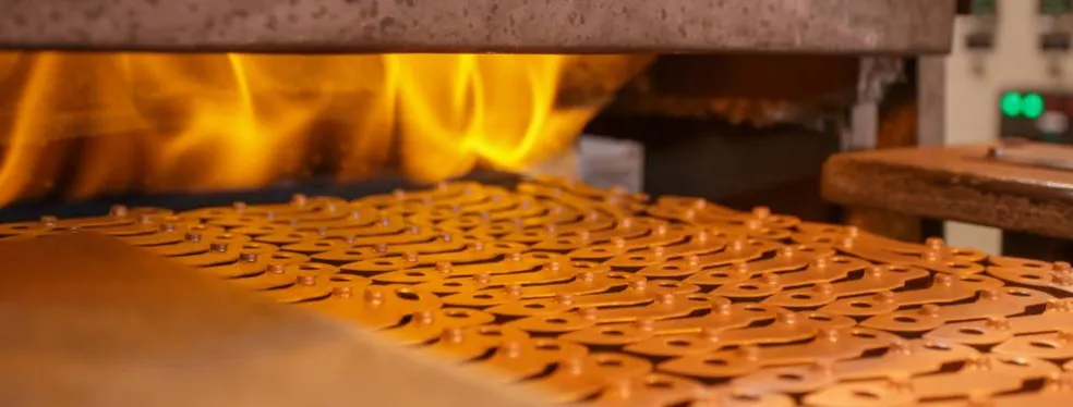 Traitement thermique de pièces métalliques par flammes sur un convoyeur industriel.