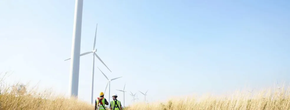 Techniciens de maintenance devant un parc éolien sous un ciel bleu.